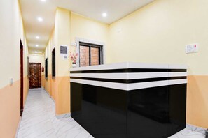 A hotel reception area with a reception desk, a door with a decorative design, and a wall-mounted light switch. - Classic Chowdhury Guest House (Barakpur)