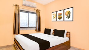 A hotel room with a bed, an air conditioning unit, a window with curtains, and three framed pictures on the wall. - Classic Chowdhury Guest House (Barakpur)