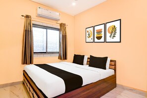 A hotel room with a bed, an air conditioning unit, a window with curtains, and three framed pictures on the wall. - Classic Chowdhury Guest House (Barakpur)