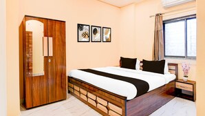 A bedroom with a wooden wardrobe, a bed with black and white bedding, a nightstand with a vase, and a window with curtains. - Classic Chowdhury Guest House (Barakpur)