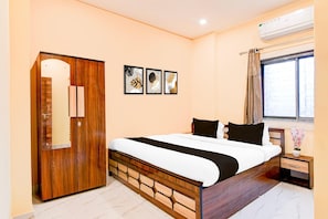 A bedroom with a wooden wardrobe, a bed with black and white bedding, a nightstand with a vase, and a window with curtains. - Classic Chowdhury Guest House (Barakpur)