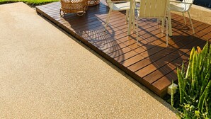 Un patio con mesa y sillas, una zona cubierta y vistas a un campo verde y árboles.