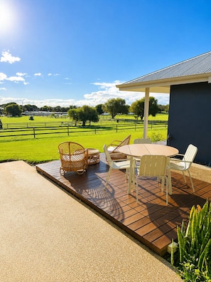 A patio with a table and chairs, a covered area, and a view of a green field and trees.