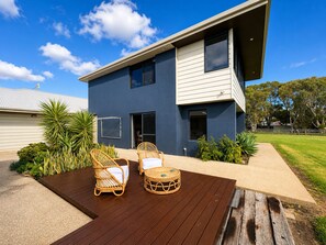A modern two-story house with a deck, outdoor furniture, and a well-maintained garden.
