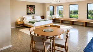 Une chambre moderne comprenant un lit, des tables de chevet, une table de salle à manger ronde avec des chaises, un banc et de grandes fenêtres offrant une vue dégagée.