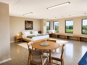 Een moderne slaapkamer met een bed, nachtkastjes, een ronde eettafel met stoelen, een bankje en grote ramen met uitzicht.