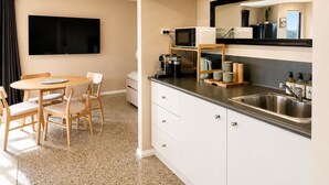 Cocina compacta con microondas, cafetera y lavamanos. Hay un comedor con mesa y sillas.