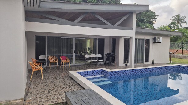 A modern house with a swimming pool, outdoor seating, and a covered patio area.