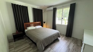 A bedroom with a bed, a nightstand, a lamp, and a window with curtains.