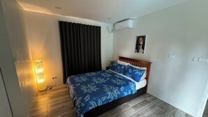 A bedroom with a bed, a wall-mounted air conditioner, a painting, and a floor lamp.
