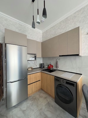 Una cocina compacta con refrigerador de acero inoxidable, horno empotrado, lavadora y pileta.