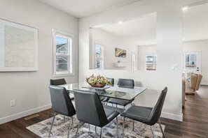 A dining area with a glass table, four chairs, a vase with flowers, and a view of the outdoors.