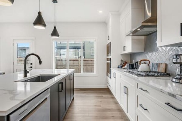 A modern kitchen with a large island, stainless steel appliances, and a view to the outside.