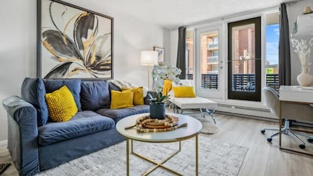 A living room with a blue sofa, a round coffee table, and a large abstract painting. - Bright Beltline Suite, Sleeps 4, Free Parking (Calgary)