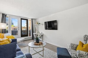 Un salon moderne comprenant un canapé, un fauteuil, une table basse et un téléviseur fixé au mur.