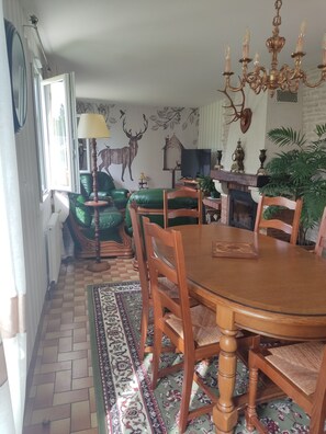A dining room with a wooden table, chairs, a chandelier, and a fireplace. - Gite La thébaïde (Thoury)
