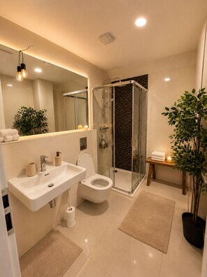 Un bagno moderno con cabina doccia in vetro, uno specchio grande, un lavandino e un water.