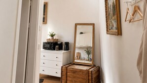 Un corridoio stretto con un lucernario, un baule di legno, un comò bianco, uno specchio e un quadro incorniciato appeso al muro.