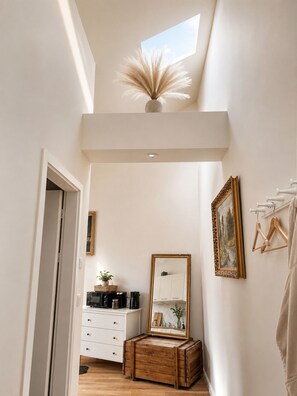 A narrow hallway with a skylight, a wooden chest, a white dresser, a mirror, and a framed painting on the wall. - Designer Sky View Loft (Prague)