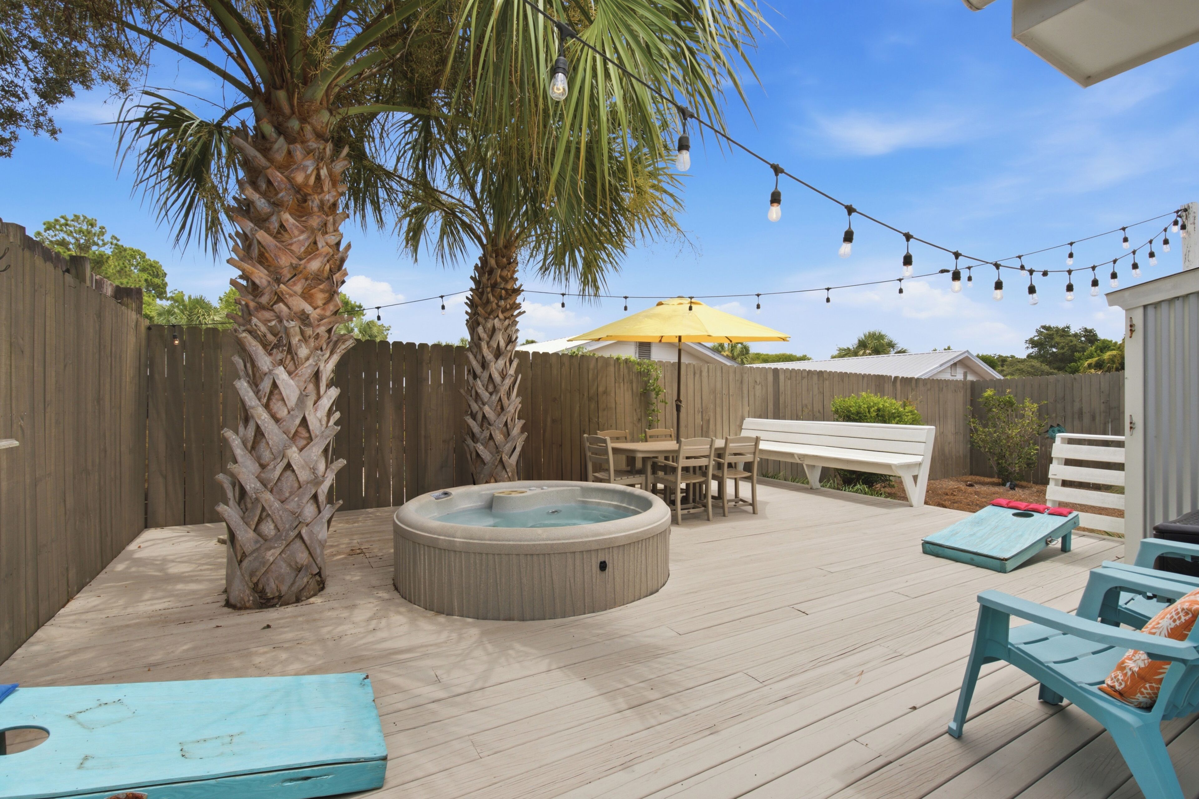 A backyard with a hot tub, wooden deck, outdoor furniture, and string lights.