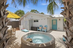 A hot tub in a backyard with a deck, outdoor furniture, and a house with a door and windows. - Bluefish House • Six-Seater Golf Cart • Walk to Beach • Private Hot Tub (Santa Rosa Beach)
