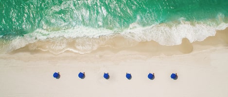 A beach with waves approaching the shore and a row of blue umbrellas aligned on the sand.