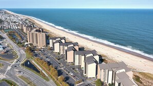 Ett bostadsområde vid kusten med höga byggnader, en strand och en väg med parkeringsplatser.