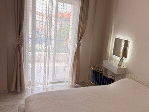 Un dormitorio con cama, mesita de noche con espejo y cortinas.