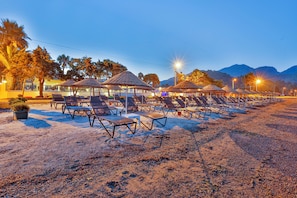 Un hotel frente a la playa con tumbonas, sombrillas y vistas a montañas.