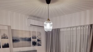 Ein ordentlich bezogenes Bett mit grauem Kopfteil, einer Hängelampe und einem großen Fenster mit Vorhängen.