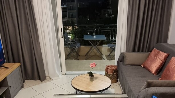 Ein modernes Wohnzimmer mit Glastisch, einer Couch und Blick durch eine Schiebetür auf einen Außenbalkon.