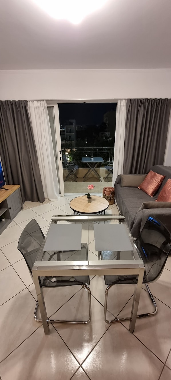 Ein modernes Wohnzimmer mit Glastisch, einer Couch und Blick durch eine Schiebetür auf einen Außenbalkon.
