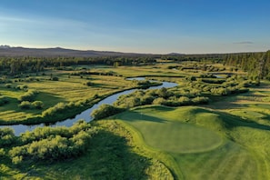 Un campo de golf con obstáculos acuáticos, abundante vegetación y montañas al fondo.