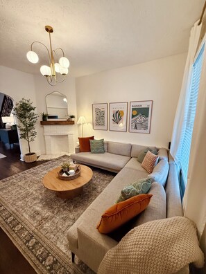A living room with a sofa, coffee table, and a fireplace. There are framed artworks on the wall and a plant in the corner. - Hot Tub | Walk to Mass Ave | Sleeps 18 | 6 BDRMS (Indianapolis)