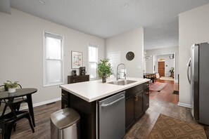 A modern kitchen with a central island, stainless steel appliances, and a dining area with a table and chairs. - Walk to Mass Ave: 2 homes, hot tub, private yard (Indianapolis)