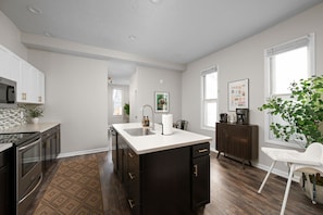 A modern kitchen with a central island, dark cabinetry, and a white countertop. - Walk to Mass Ave: 2 homes, hot tub, private yard (Indianapolis)