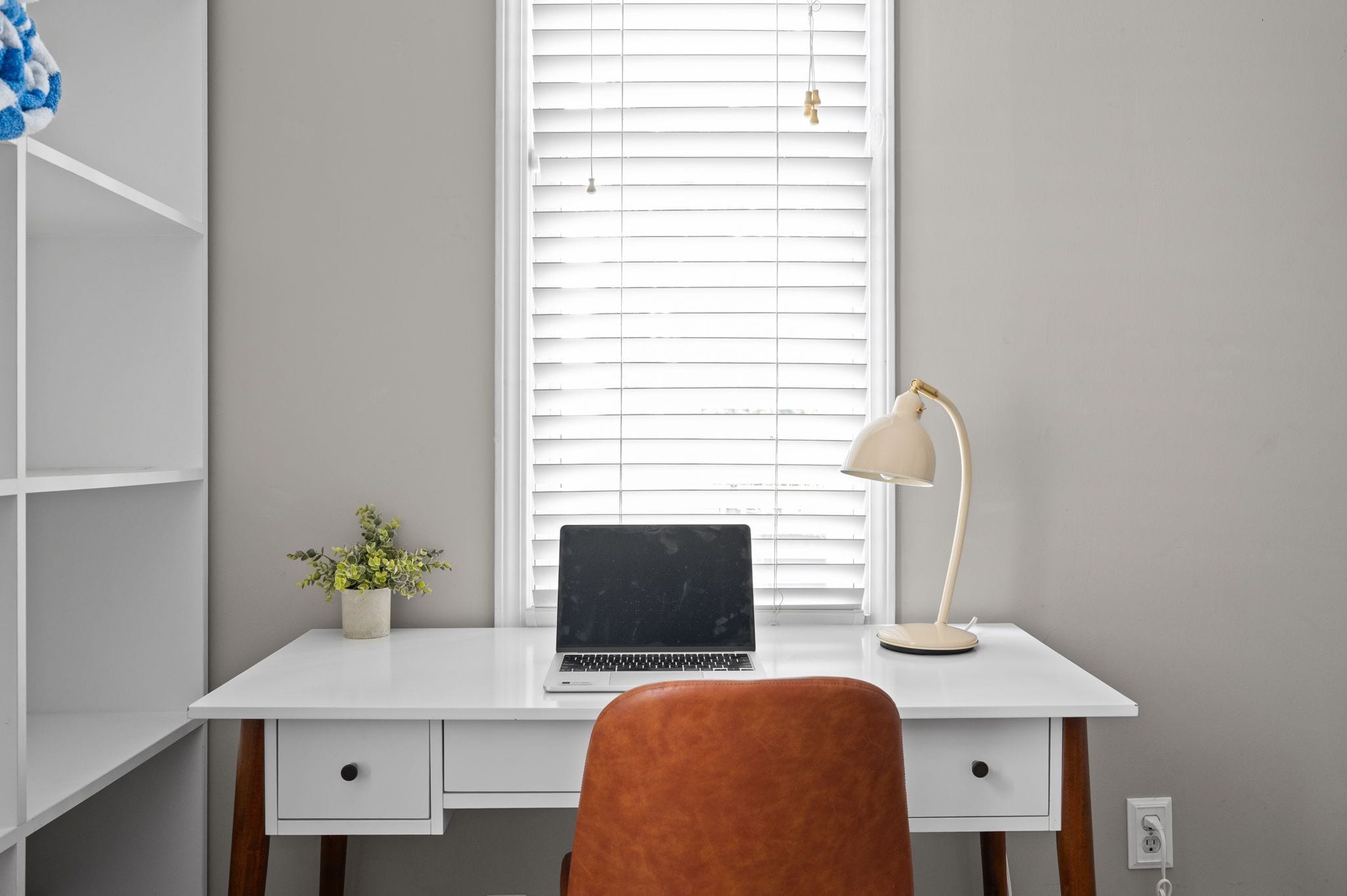 A white desk with a laptop, a desk lamp, and a potted plant.