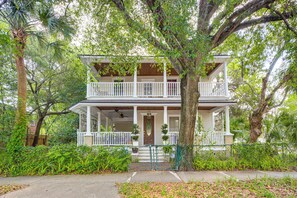 A two-story house with a porch, surrounded by trees and greenery.