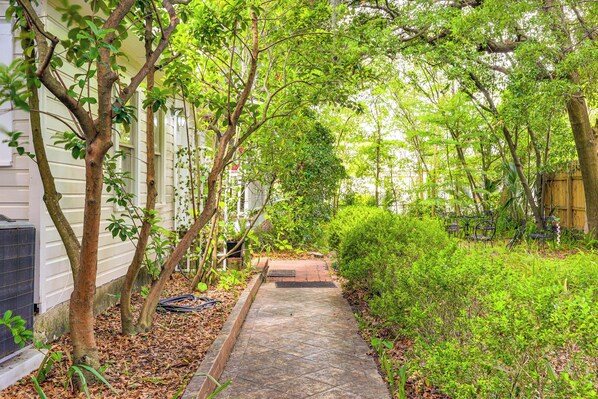 A pathway leading to a house with a covered porch, surrounded by greenery and a wooden fence.