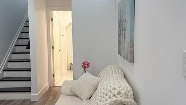 Un salon moderne avec un canapé blanc, un plancher en bois, un escalier et une porte donnant sur une autre pièce.