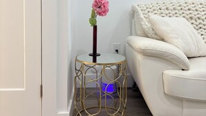 Un canapé blanc avec un coussin blanc, une petite table ronde avec une fleur rose, et un tableau accroché au mur.