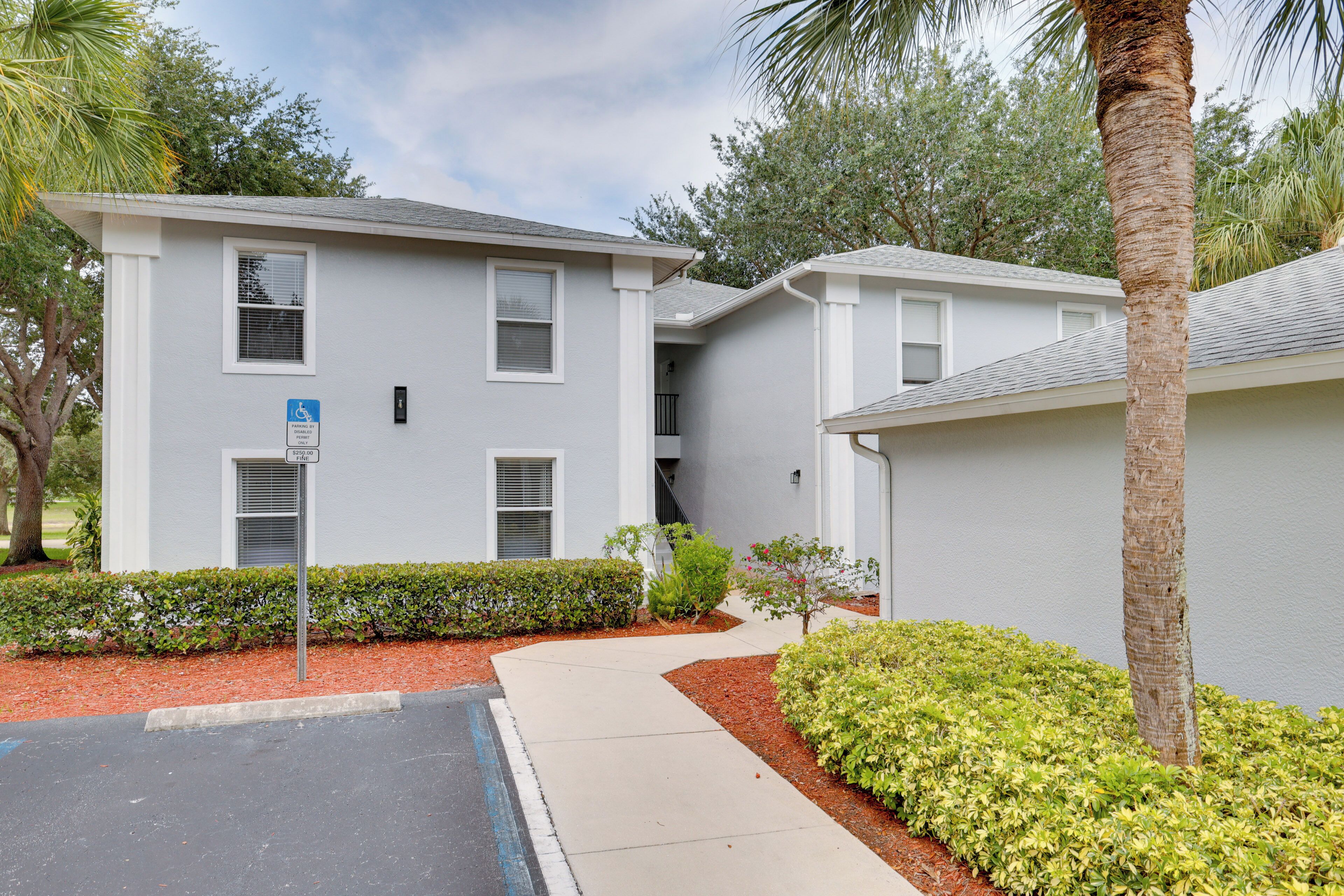 A two-story building with a parking lot, a wheelchair-accessible sign, and a palm tree.