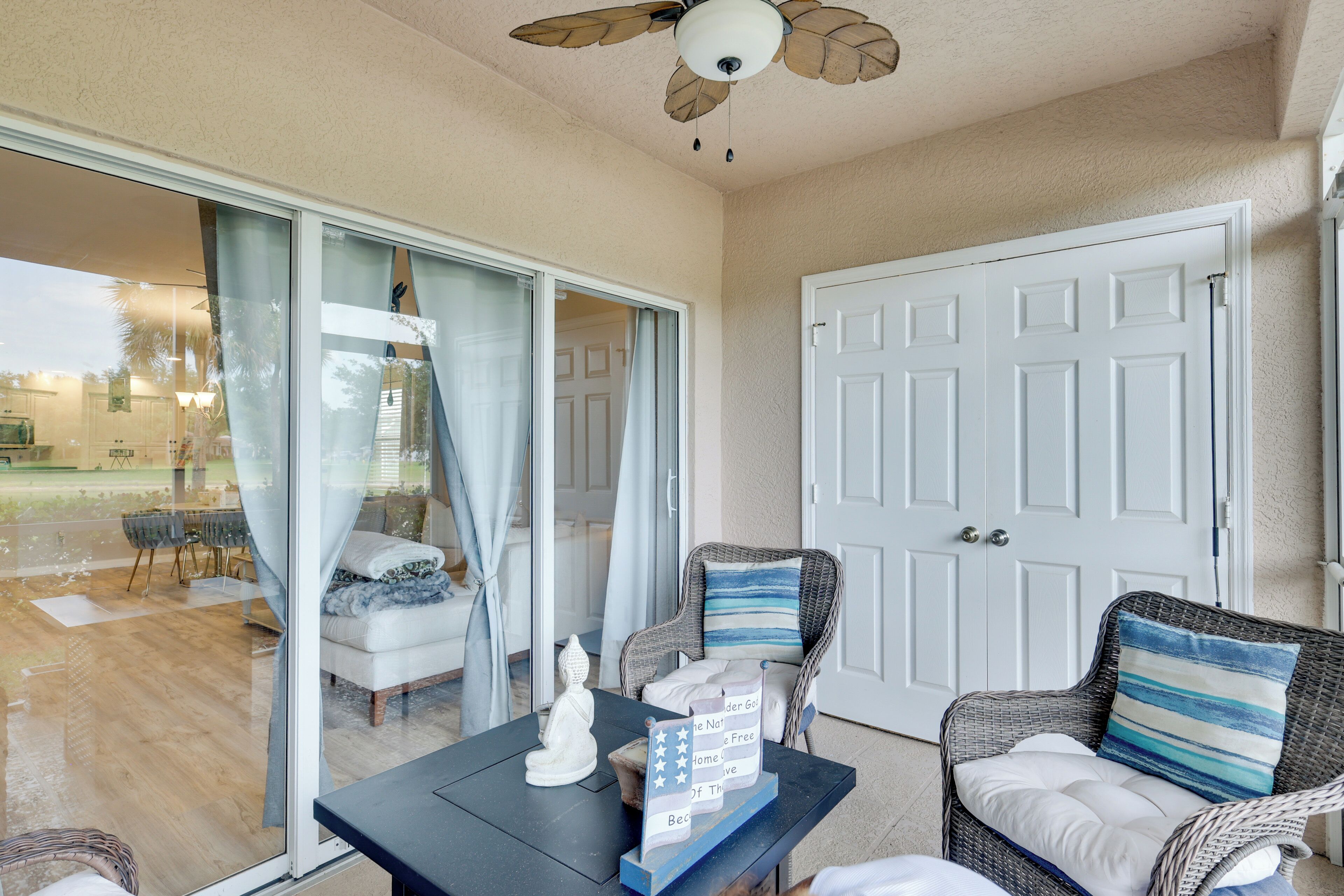 A room with a sliding glass door leading to an outdoor area, a wicker chair with a pillow, a small table with a decorative item, and a ceiling fan.