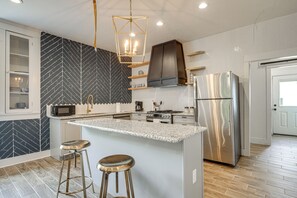 Eine moderne Küche mit Kochinsel, Barhocker, einem Edelstahl-Kühlschrank und einer Mikrowelle.