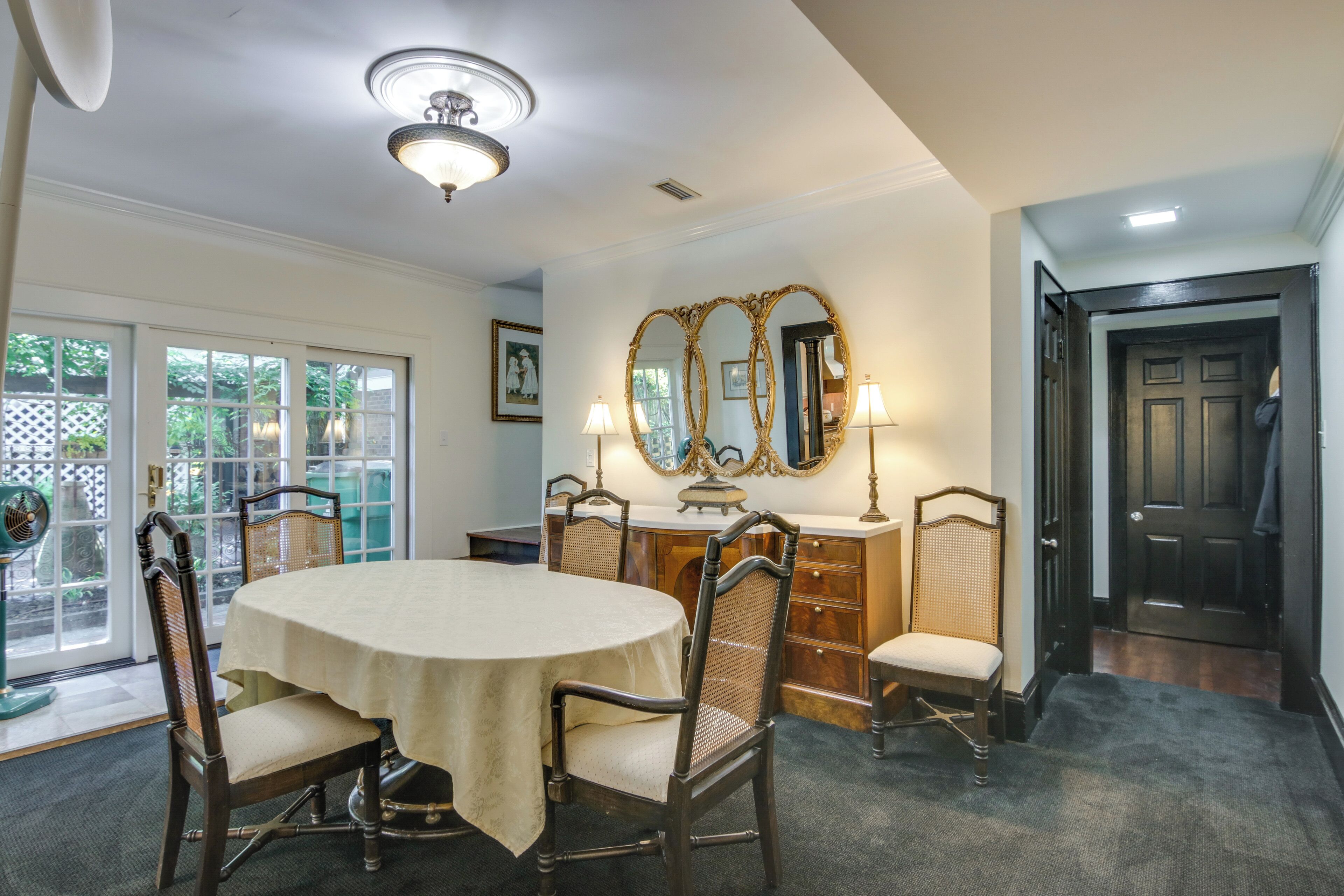 Une salle à manger avec une table ronde, des chaises, un lustre et un grand miroir.