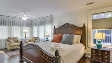 A bedroom with a large bed, a nightstand with a lamp, a chair, and a window with blinds.
