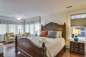 Ein Schlafzimmer mit einem großen Bett, einem Nachttisch mit Lampe, einem Sessel und einem Fenster mit Jalousien.