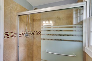 A shower with a glass door, a handrail, and a tiled wall with a decorative border. - Home w/ Fenced Yard, 13 Mi to Kansas City Stadium! (Kansas City)