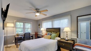 A bedroom with a bed, bedside tables, a desk, a chair, a ceiling fan, and a window with blinds. - KC Stadium Gateway: Home w/ Private Yard (Kansas City)