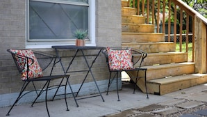 A patio with two metal chairs and a table, a wooden staircase, and a brick wall. - KC Stadium Gateway: Home w/ Private Yard (Kansas City)
